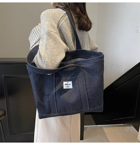 Detail shot of a large denim tote bag featuring a branded label and striped inner lining