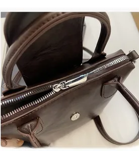 Close-up of the smooth silver zipper and magnetic buckle on the brown leather handbag