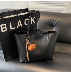 Détail d'un sac cabas en cuir noir avec un charmant ours en peluche sur un canapé noir