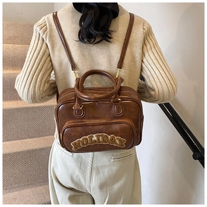 Brown faux leather backpack showing plush 'HOLIDAY' letter patch and adjustable straps