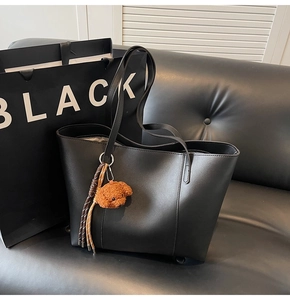 Détail d'un sac cabas noir mat avec un pendentif chien en peluche sur canapé en cuir