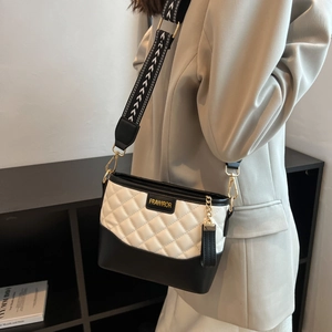 Close-up of black and white quilted crossbody bag with gold logo and wide patterned strap