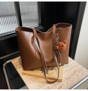 Détail d'un sac cabas marron foncé en similicuir avec bandoulières et bijou d'ours