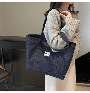 Detailed close-up of dark blue denim tote bag featuring a stitched white brand logo patch