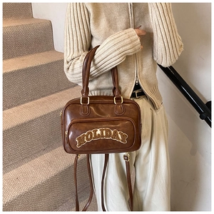 Detail of vintage brown PU leather handbag with HOLIDAY embroidery on a staircase