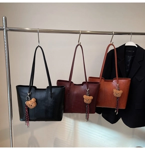 Close-up of retro leather tote bags in black, burgundy, and brown with cute bear pendants
