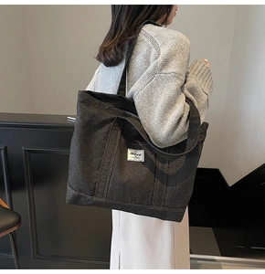 Detailed texture of black denim tote bag with stitched rectangular logo and wide strap