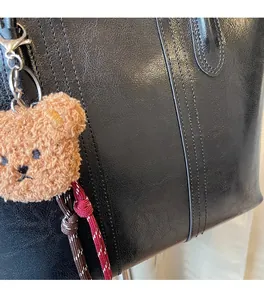 Detail of black leather tote bag with vertical stitching and cute brown plush bear charm
