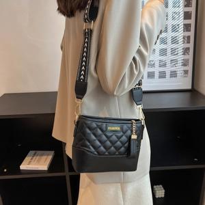 Detail of black quilted crossbody bag with letter logo and woven shoulder strap