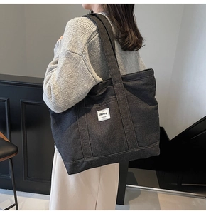 Detail shot of a black denim tote bag with white woven label and sturdy shoulder strap
