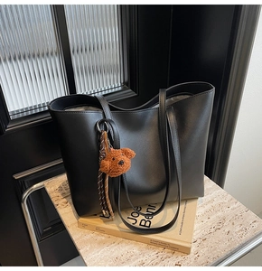 Détail d'un grand sac cabas noir en similicuir mat avec un charm d'ours en peluche