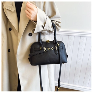 Detail of a vintage black leather shell bag with gold rings shown on a beige trench coat