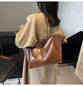 Borsa tote in pelle marrone con scritta VVGONGZYD abbinata a un trench color beige
