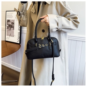 Chic black faux leather shell bag with gold hardware shown on light coat outfit