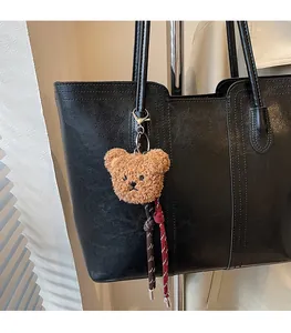 Close-up of plush brown bear charm with braided tassels on black leather tote bag