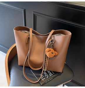 Détail du sac cabas en cuir marron caramel avec breloque ours en peluche sur chaise