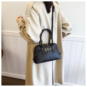 Detail of black Boston bag with gold hardware and dual handles shown on an overcoat