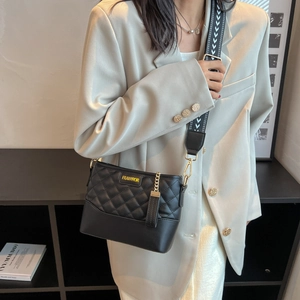 Quilted black crossbody bag with a wide geometric strap and gold chain detail on model
