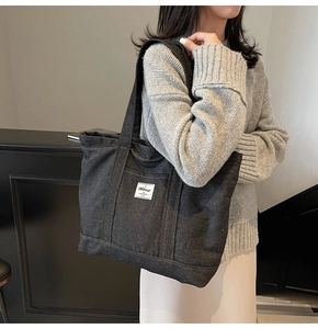 Detail of dark gray denim tote bag with Hbag logo patch worn by a model