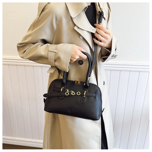 Detail of retro black shell bag with gold rings and cylindrical handles on beige trench coat
