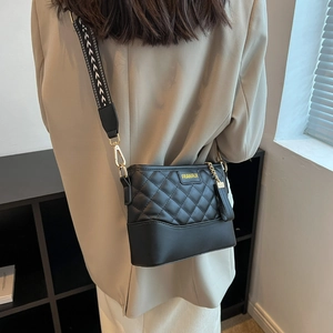 Close-up of black quilted leather crossbody bag featuring a wide geometric strap and fringe