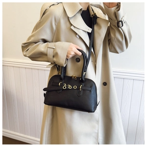 Detail of vintage black shell bag with golden hardware and bottom rivets on a beige trench coat