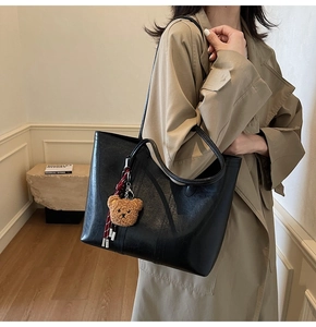 Close-up of large black leather tote bag with a cute brown bear charm on model