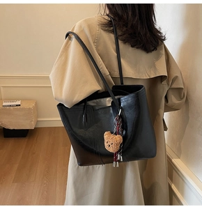 Rear view of a minimalist black tote bag with plush bear charm on a beige trench coat