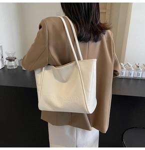 Dettaglio del logo in rilievo sulla borsa tote grande bianco crema indossata da modella