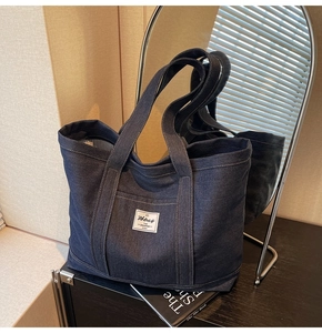 Close-up of deep blue denim tote bag featuring a white brand label and striped lining