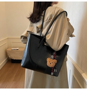 Detail view of large black tote bag with plush bear charm and ribbon on model shoulder