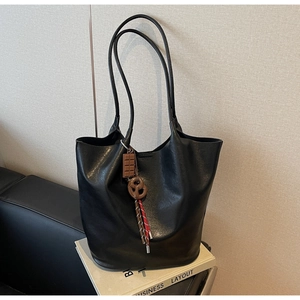 Gros plan du sac cabas en cuir noir avec des breloques chocolat posé sur un livre blanc