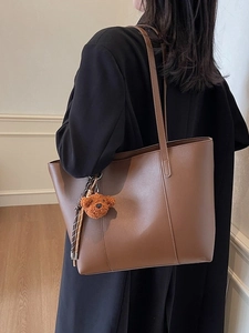 Sac fourre-tout marron en similicuir avec bandoulières et breloque ours sur modèle