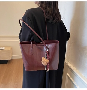 Detail of burgundy leather tote bag featuring a cute plush bear charm and shoulder straps