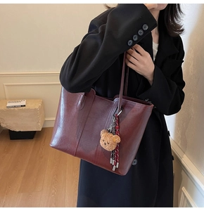Detail of burgundy leather tote bag featuring a cute plush bear and tassel charm