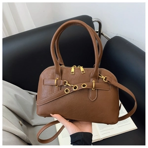 Detailed view of brown shell bag with golden hardware and adjustable strap on books