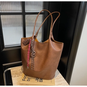 Détail d'un sac cabas en cuir marron avec breloque chocolat et lanières tissées décoratives