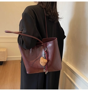 Detailed view of a burgundy leather tote bag with a plush bear charm and striped cord