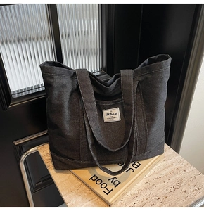 Detailed macro view of dark grey denim tote bag with dual straps and woven brand label