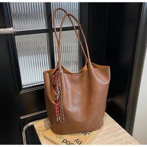 Détail macro du sac cabas en cuir texturé marron foncé avec pompon décoratif et bandoulière