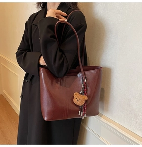 Detail of burgundy leather tote bag with plush bear charm on a model in a black coat