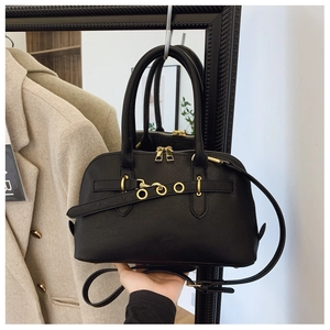 Detail of black pebbled leather shell bag with gold round buckle and zipper closure