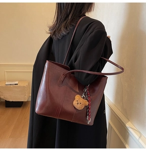 Detail of burgundy leather tote bag with a small bear pendant for office commute