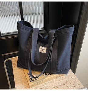 Detail of dark blue denim tote bag with white stitching and brand label on a book