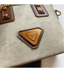 Détail du sac vert sauge avec logo métallique triangulaire et rivets dorés élégants