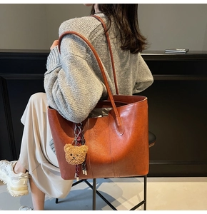 Detailed back view of a retro brown leather tote bag with a cute plush bear charm