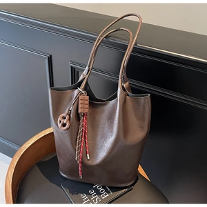 Détail d'un sac cabas en cuir marron foncé avec breloques chocolat sur une chaise noire