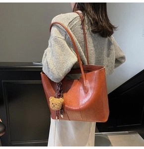Detail view of a vintage tan tote bag featuring a cute teddy bear charm on shoulder