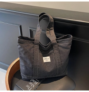 Detailed shot of dark grey denim tote bag with white woven label and reinforced stitching