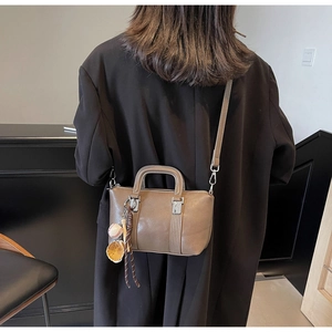 Détail du sac bandoulière taupe avec breloque baseball sur fond de manteau en laine